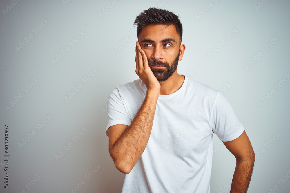 Young indian man wearing t-shirt standing over isolated white background thinking looking tired and bored with depression problems with crossed arms. Young indian man wearing t-shirt standing over isolated white background thinking looking tired and bored with depression problems with crossed arms.