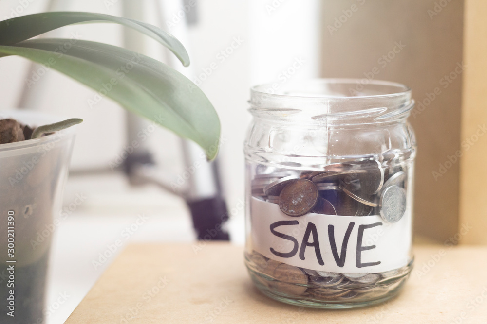 Jar with coins and inscription SAVE. Economy and finance prosperity concept. Saving income and money management idea, represented by a jar full of metalic coins on modern background. Jar with coins and inscription SAVE. Economy and finance prosperity concept. Saving income and money management idea, represented by a jar full of metalic coins on modern background.