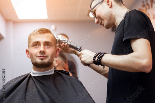 handsome guy makes a short haircut in a barbershop with a trimmer, close-up