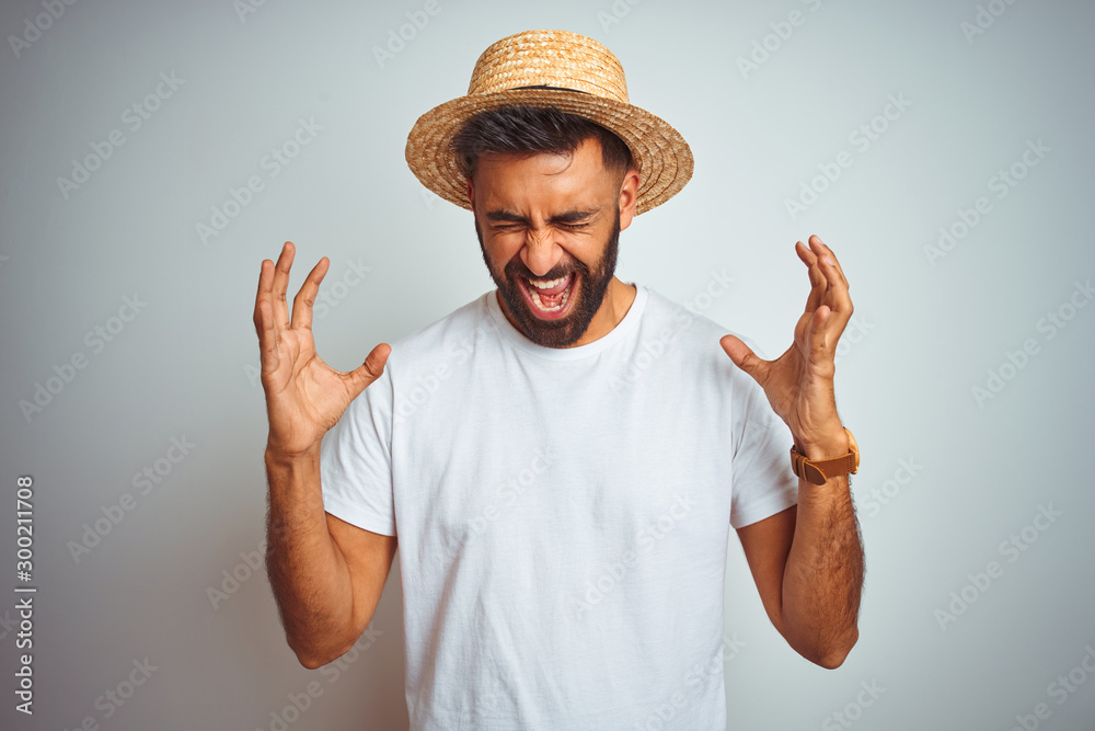 Young indian man on holiday wearing summer hat standing over isolated white background celebrating mad and crazy for success with arms raised and closed eyes screaming excited. Winner concept Young indian man on holiday wearing summer hat standing over isolated white background celebrating mad and crazy for success with arms raised and closed eyes screaming excited. Winner concept