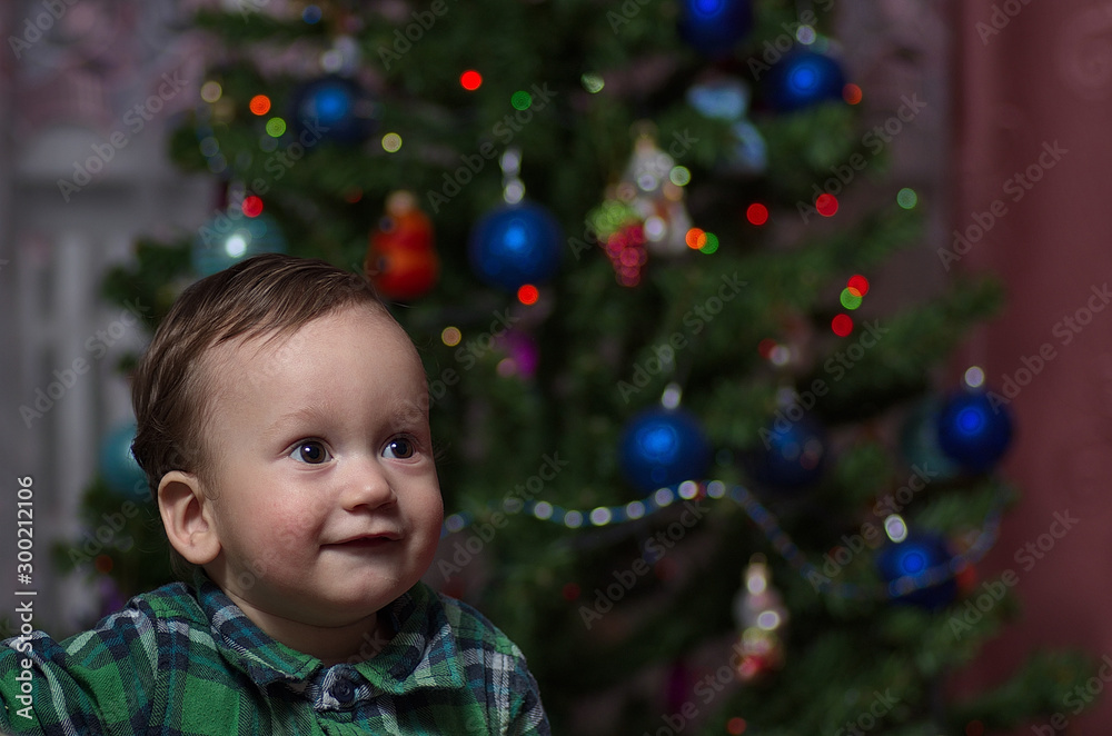 A little boy stands at the Christmas tree.