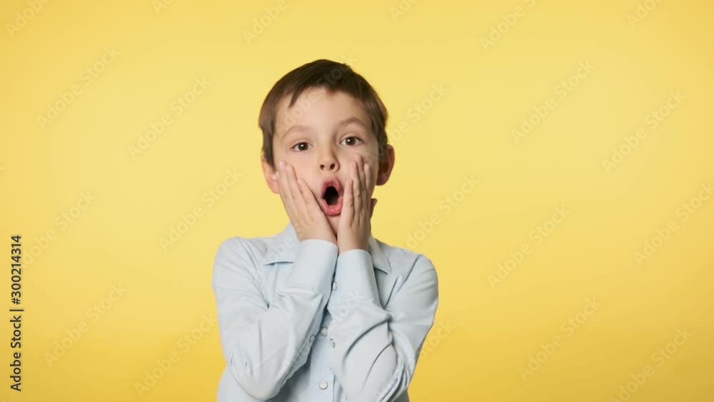 Cute boy kid surprised with hands on his face. Caucasian boy in blue shirt doing silly funny face at yellow background. 4k, UHD 60FPS slow motion Cute boy kid surprised with hands on his face. Caucasian boy in blue shirt doing silly funny face at yellow background. 4k, UHD 60FPS slow motion