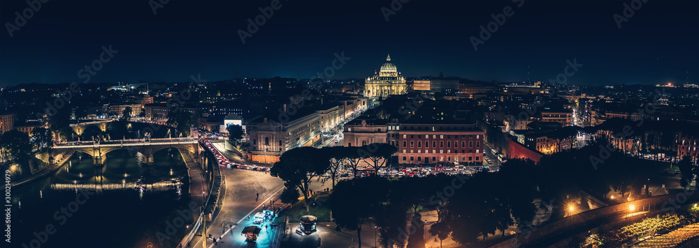 St Angel Bridge on Tiber river and St. Peter Basilica in Vatican City at night with city illumination in Rome, Italy, view from above, panorama.