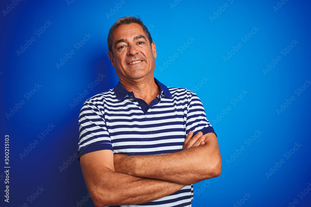 Handsome middle age man wearing striped polo standing over isolated blue background happy face smiling with crossed arms looking at the camera. Positive person. Handsome middle age man wearing striped polo standing over isolated blue background happy face smiling with crossed arms looking at the camera. Positive person.