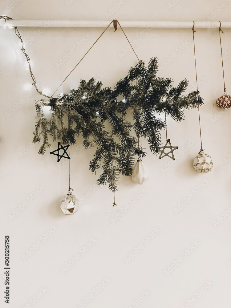 Stylish christmas tree branch with lights and glass ornaments hanging on  white wall. Modern eco decoration in scandinavian style on white rural  wall. Happy Holidays. Festive decor Stock Photo | Adobe Stock