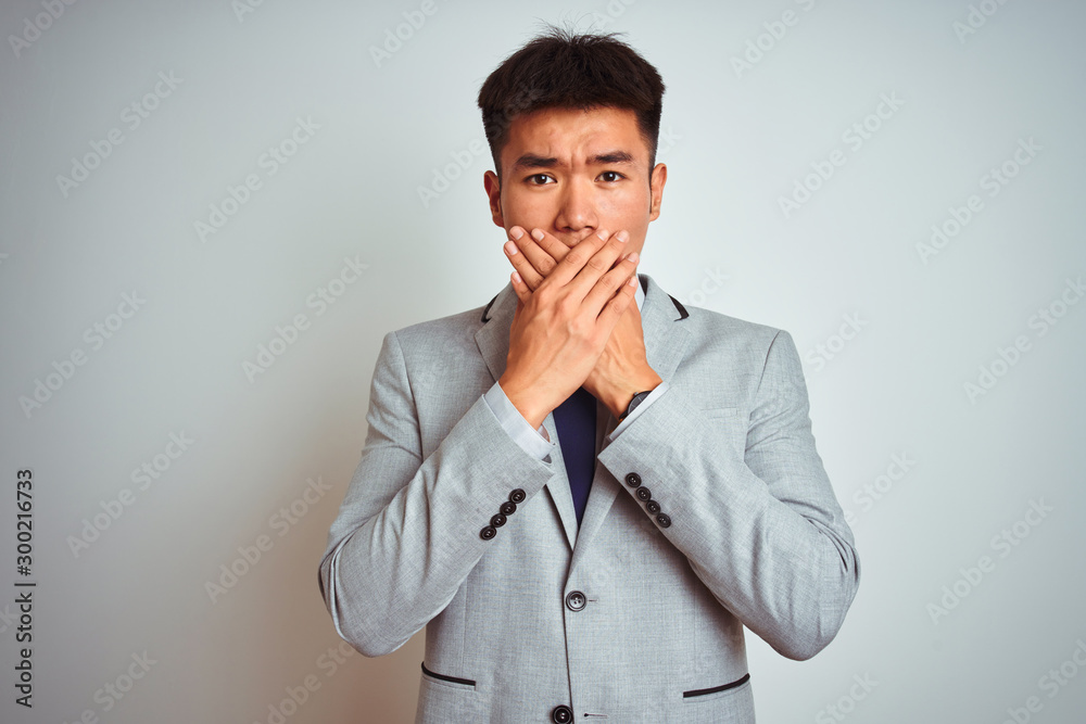Asian chinese businessman wearing suit and tie standing over isolated yellow background shocked covering mouth with hands for mistake. Secret concept. Asian chinese businessman wearing suit and tie standing over isolated yellow background shocked covering mouth with hands for mistake. Secret concept.