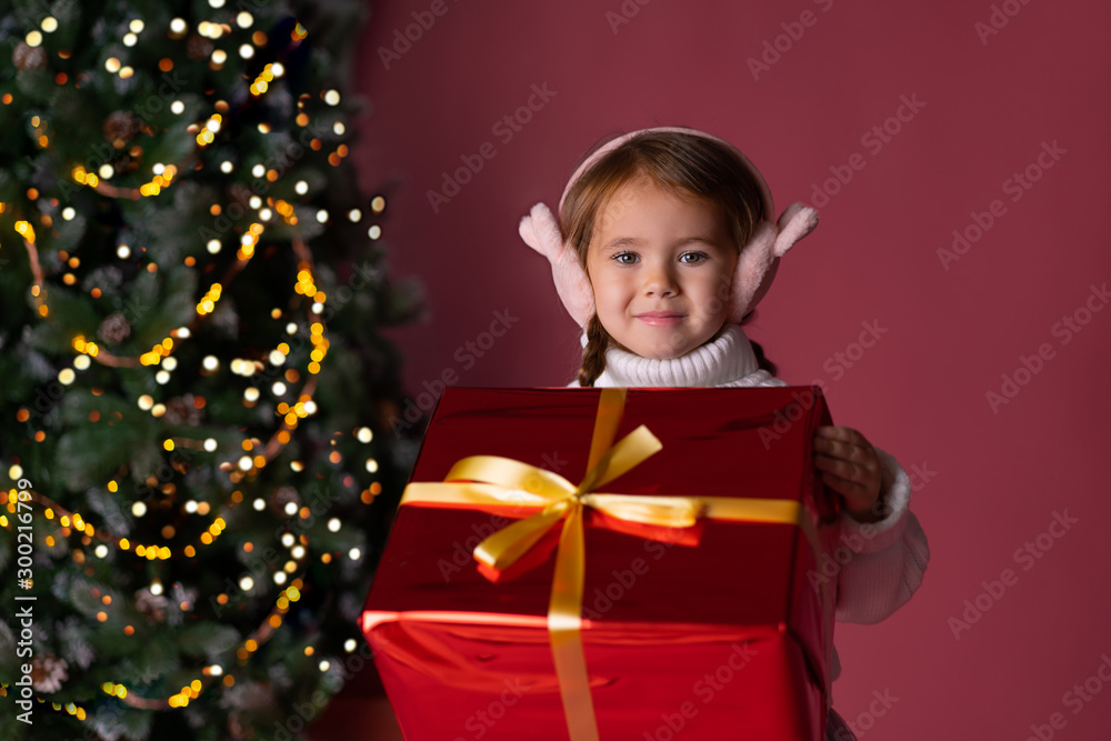 Beautiful little girl in the hat sitting near presents and christmas tree. Bokeh lights on the background. Concept christmas Beautiful little girl in the hat sitting near presents and christmas tree. Bokeh lights on the background. Concept christmas