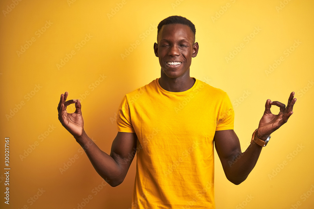 Young african american man wearing casual t-shirt standing over isolated yellow background relaxed and smiling with eyes closed doing meditation gesture with fingers. Yoga concept.
