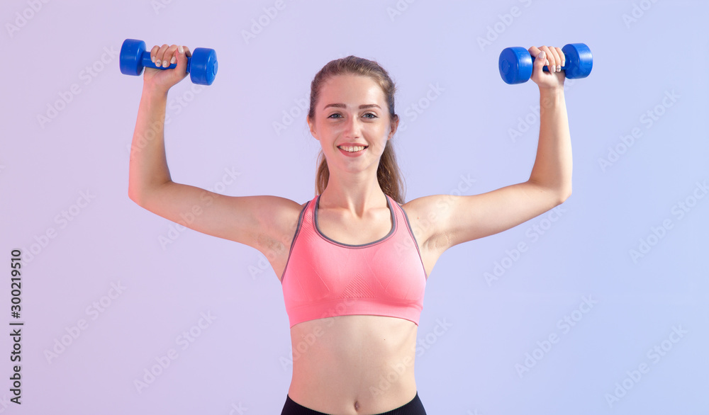 Young fitness woman. Female doing exercises with two dumbbells standing on a pink purple background. Young fitness woman. Female doing exercises with two dumbbells standing on a pink purple background.