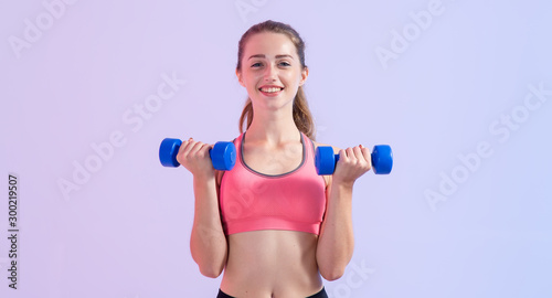 Young fitness woman. Female doing exercises with two dumbbells standing on a pink purple background.