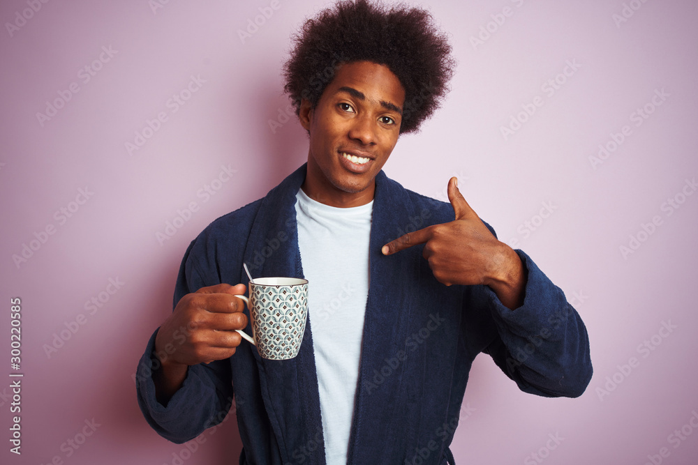 Afro american man wearing pajama drinking coffee standing over isolated pink background with surprise face pointing finger to himself - obrazy, fototapety, plakaty 