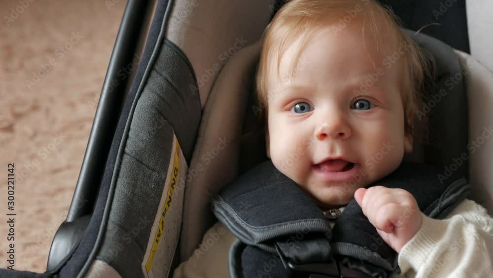 The baby sits in a car seat. A young child lies in a car seat and laughs.