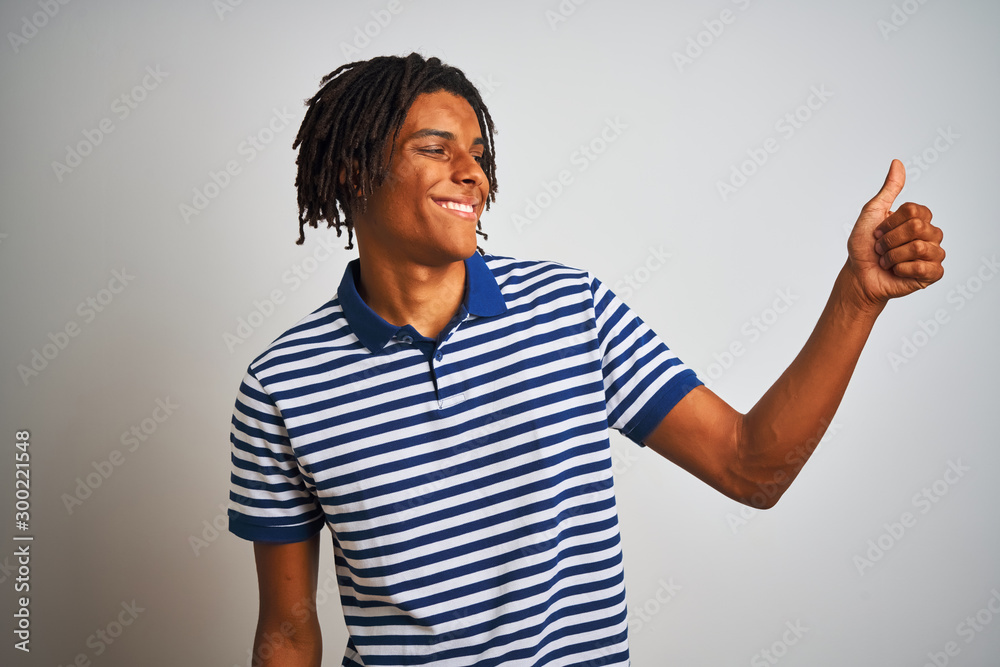 Afro man with dreadlocks wearing striped blue polo standing over isolated white background Looking proud, smiling doing thumbs up gesture to the side Afro man with dreadlocks wearing striped blue polo standing over isolated white background Looking proud, smiling doing thumbs up gesture to the side