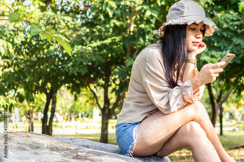 Young happy woman using smartphone. Beautiful smiling woman use of mobile phone in public park. © lllonajalll