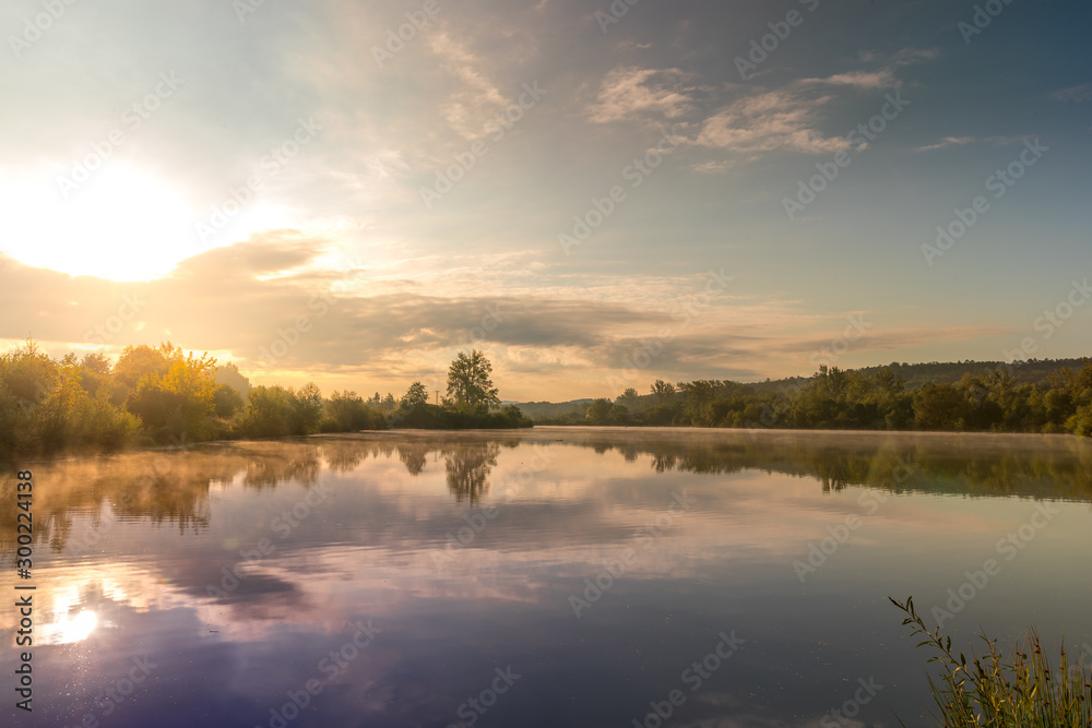 Sunset capture on the pond at the morning sunrise over trees lying near water and moving clouds over water with reflection on water surface. Sunset capture on the pond at the morning sunrise over trees lying near water and moving clouds over water with reflection on water surface.