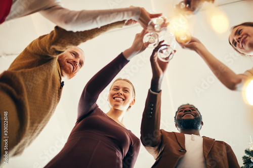 Low angle view at multi-ethnic group of people e clinking champagne glasses during Christmas party, copy space photo