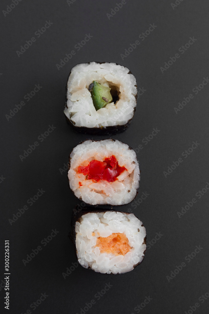 Set of three sushi rolls with fish, avocado and cheese on black background isolated. Traditional japanese food. Asian restaurant meals delivery. Set of three sushi rolls with fish, avocado and cheese on black background isolated. Traditional japanese food. Asian restaurant meals delivery.