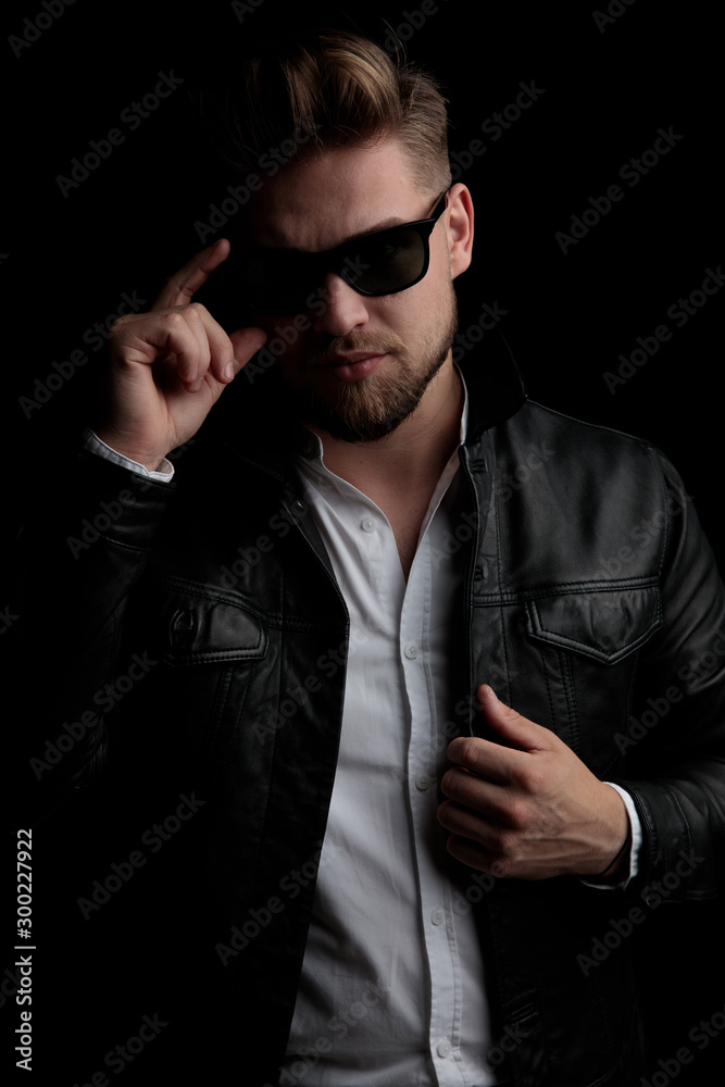 casual man standing and fixing his sunglasses and jacket