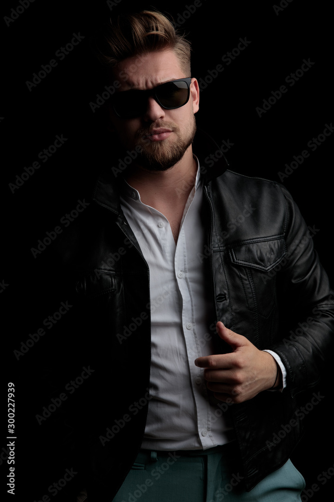Obraz premium casual man wearing sunglasses standing and fixing his leather jacket