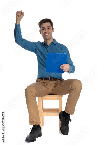 happy young man holding clipboard and celebrating victory