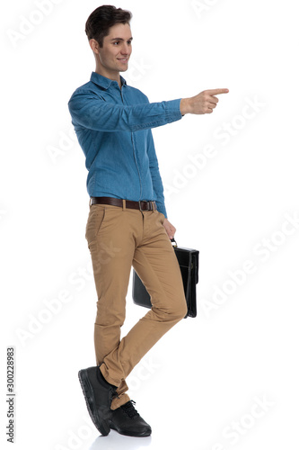 happy young man holding suitcase and pointing finger