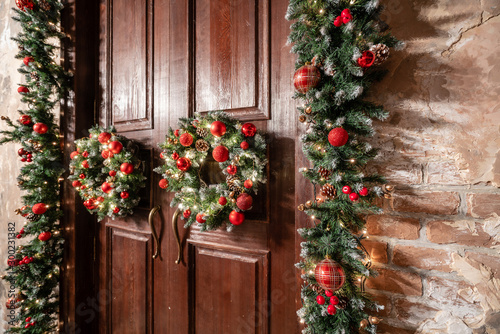House entrance decorated for holidays. Christmas decoration. Two wreaths and garland of fir tree branches. Large wooden door