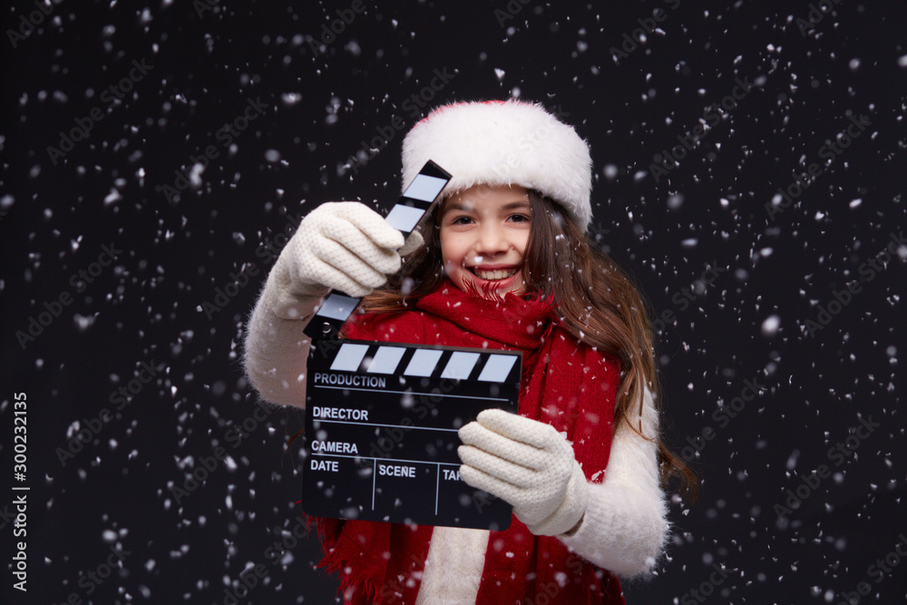 Young beautiful smiling girl in knitting pullover holding director's clapper board for making Christmas video in studio.Movie production clapper board.Lights, camera, action. Start of winter holidays. Young beautiful smiling girl in knitting pullover holding director's clapper board for making Christmas video in studio.Movie production clapper board.Lights, camera, action. Start of winter holidays.