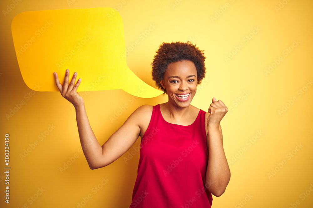 Young african american woman holding speech bubble over yellow isolated background screaming proud and celebrating victory and success very excited, cheering emotion Young african american woman holding speech bubble over yellow isolated background screaming proud and celebrating victory and success very excited, cheering emotion