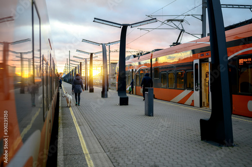 People boarding trains at the train stop or railway station. Two platform tracks both have a train with an open doors ready for boarding passengers.