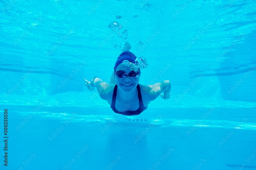 Young girl swimming underwater in the pool, female looking and smiling