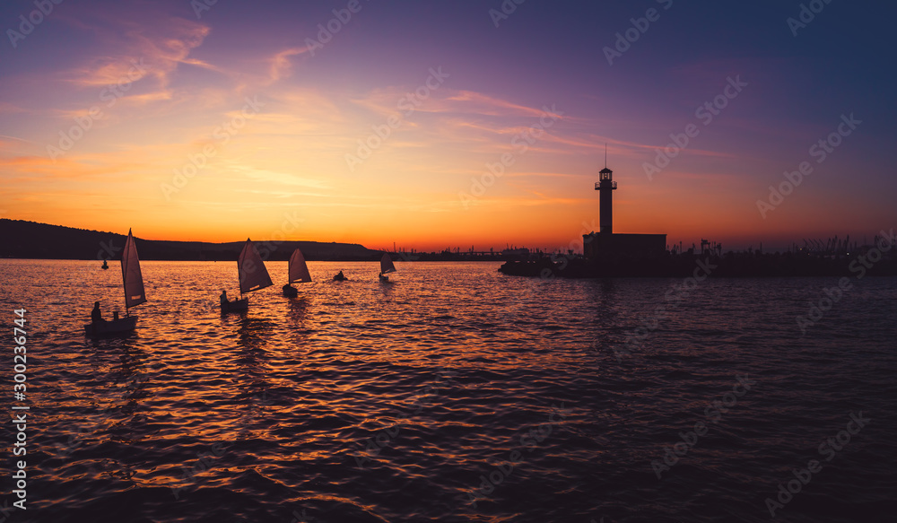 Sailing wind boats at sunset near lighthouse and sea port Varna, Bulgaria. Sport competition.