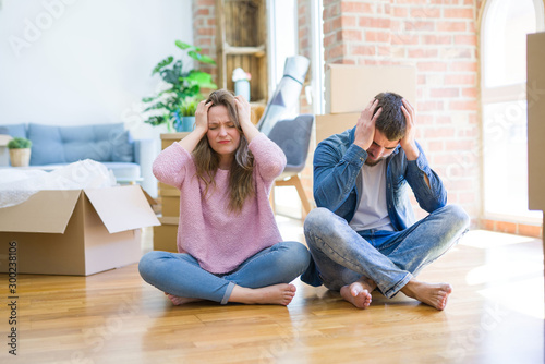 Fotografie Young beautiful couple moving to a new house sitting on the floor suffering from headache desperate and stressed because pain and migraine