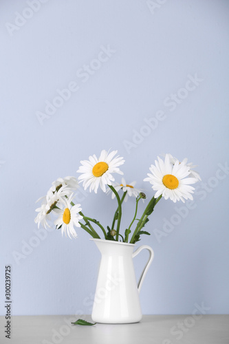 Beautiful tender chamomile flowers in jug on table against light background © New Africa
