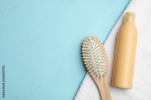 Flat lay composition with brush and shampoo bottle on light blue background  space for text. Hair care cosmetics