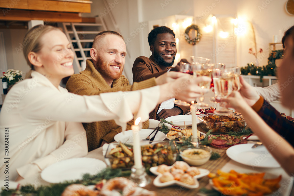 © Seventyfour - Multi-ethnic group of people raising glasses while celebrating Christmas with friends and family sitting at beautiful dinner table