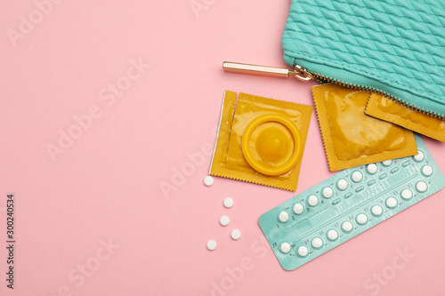 Condoms and birth control pills in purse on pink background, top view with space for text. Safe sex photo