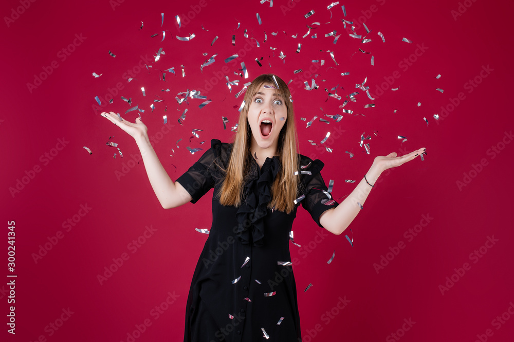excited happy woman throws silver confetti in the air wearing dress isolated over red