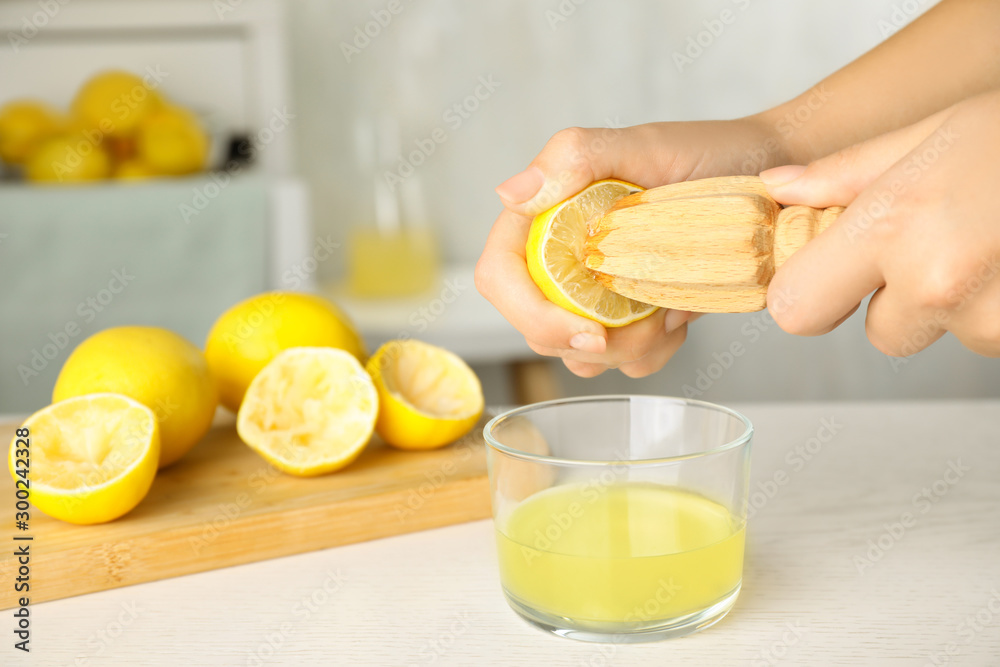 Woman squeezing lemon juice with reamer at white wooden table, closeup. Space for text - obrazy, fototapety, plakaty 