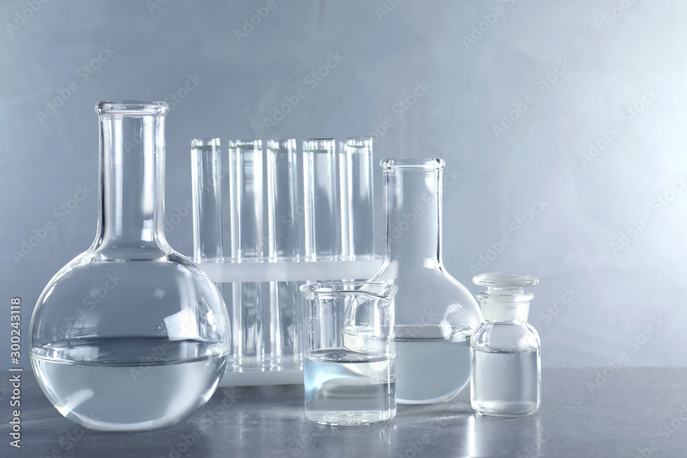 Laboratory glassware with liquid samples for analysis on table against grey background Laboratory glassware with liquid samples for analysis on table against grey background