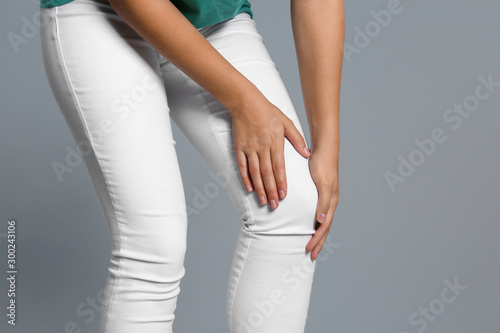 Woman suffering from knee pain on grey background, closeup