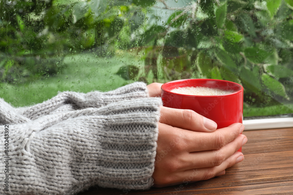 Woman with cup of coffee near window on rainy day, closeup - obrazy, fototapety, plakaty 