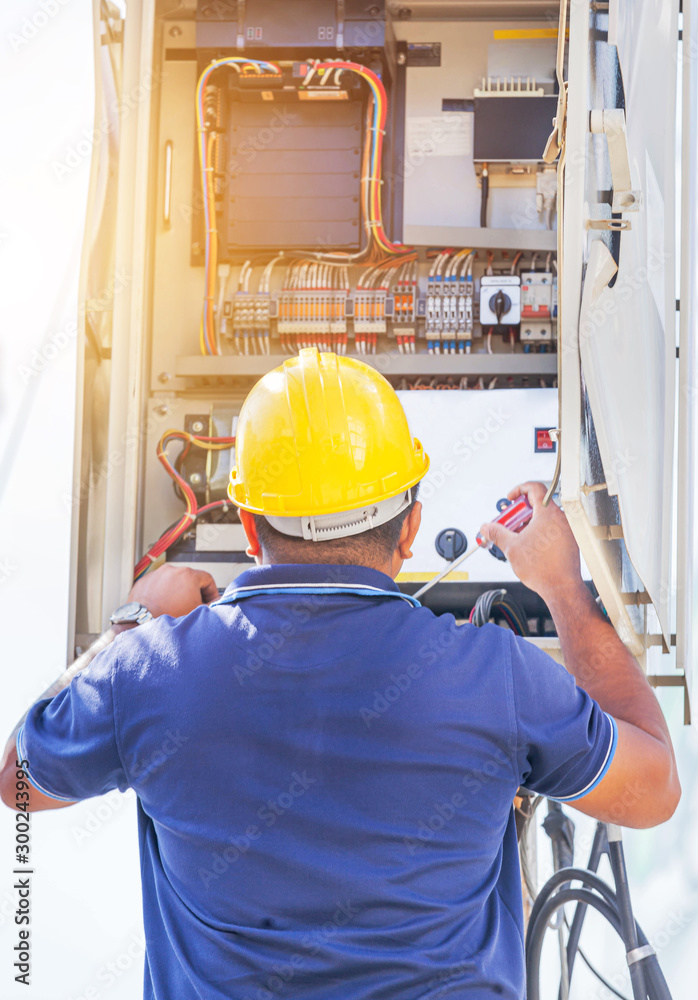 Electrician with yellow safety helmet screwing equipment repairing in fuse circuit breaker box Electrician with yellow safety helmet screwing equipment repairing in fuse circuit breaker box