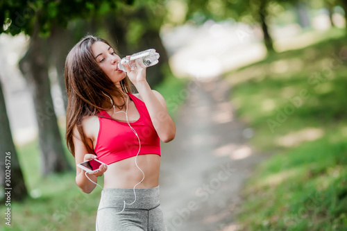 Young woman running outdoors in park with bottle of water and phone in hands.