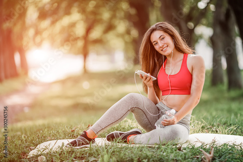 Young sporty woman resting in the park after training and using the phone.