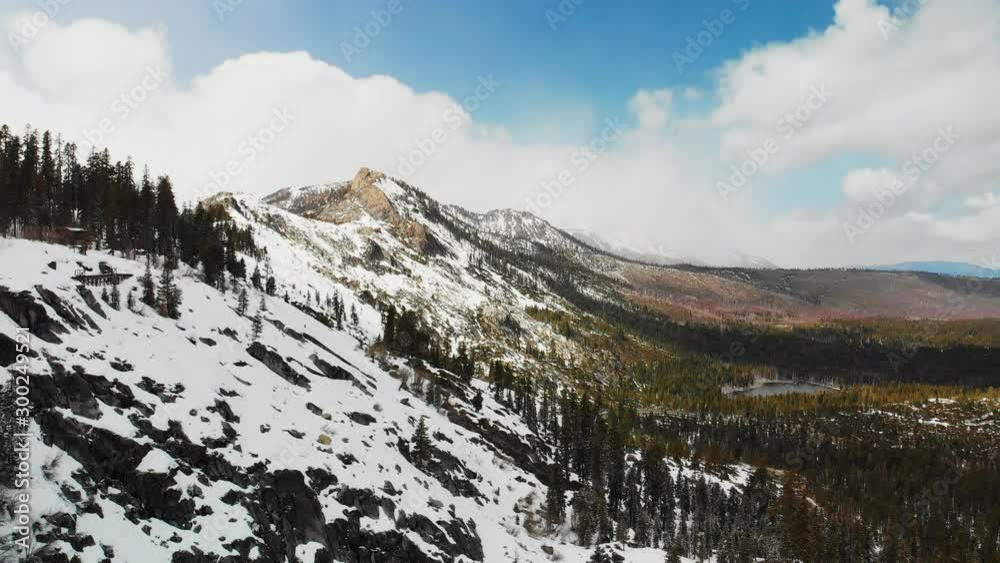 Aerial drone shot along a snowy mountain ridge on a partially cloudy day near South Lake Tahoe