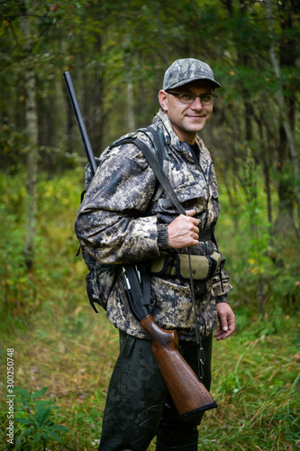 Hunter wearing glasses and camouflage with weapon shotgun at the outdoor hunting