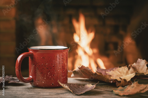 Red mug with hot tea in front of a burning fireplace, comfort and warmth of the hearth concept