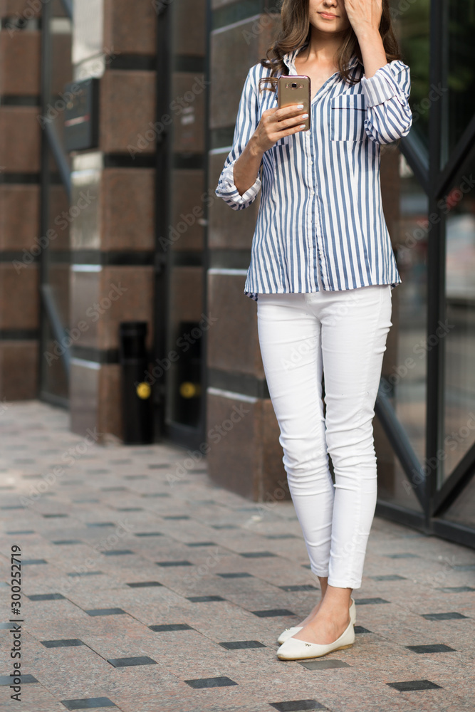 Businesswoman uses a mobile phone, walking along the city streets with coffee in her hand.