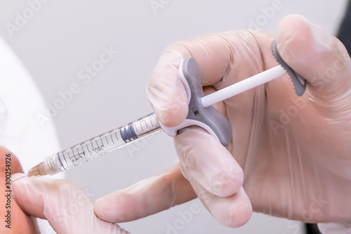 Gloved doctor hand injecting a vial of hyaluronic acid (HA) based dermal filler into patient for a non-surgical cheek and face lift.