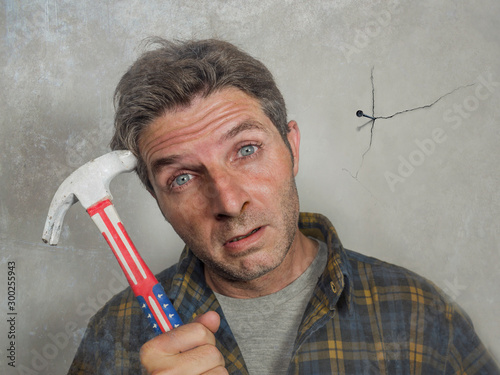 фотографія funny portrait of man holding hammer after driving a nail for hanging a frame bu